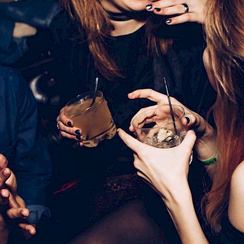 People are enjoying a night out, holding drinks and laughing together in a lively social setting.