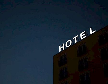 A building shows a partially lit neon sign reading "HOTEL" against a dark sky, with only some letters illuminated.