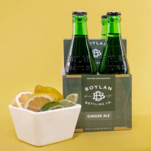 Four bottles of Boylan Ginger Ale in a green carrier with a bowl of sliced lemon, lime, and orange on the side.