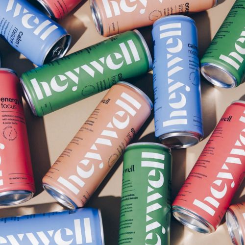 The image shows various colorful cans with the label "heywell" in green, blue, pink, and peach shades scattered on a surface.