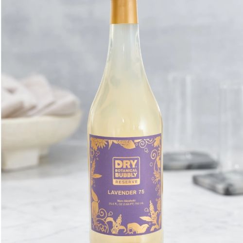A bottle of Dry Botanical Bubbly Lavender 75 is on a counter, with a purple and gold label featuring decorative floral designs.
