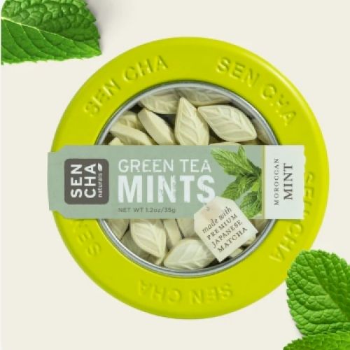 A round tin labeled "Green Tea Mints" with leaf-shaped mints inside and mint leaves around it.