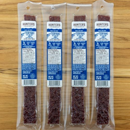 The image shows four packages of Hunter's Reserve Teriyaki beef sticks laid out on a wooden surface.