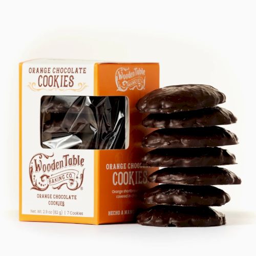 A box of Wooden Table orange chocolate cookies with a stack of cookies beside it, showcasing the packaging and treats.