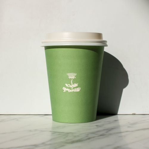 A green paper cup with a white lid sits on a marble surface, featuring a simple logo design in white.