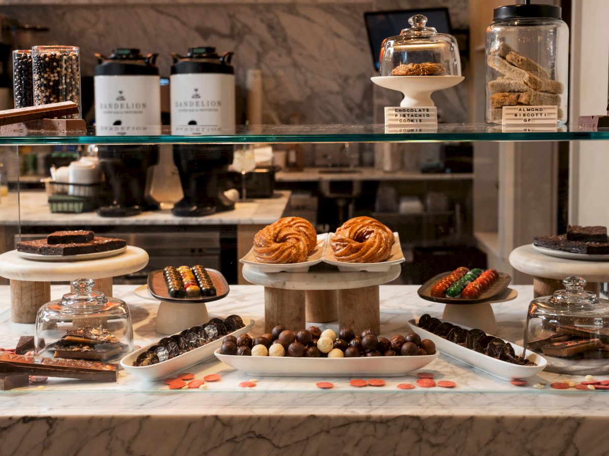 A dessert buffet display with assorted chocolates, truffles, cookies, and colorful candies on glass stands, topped with jars and cookie tins.